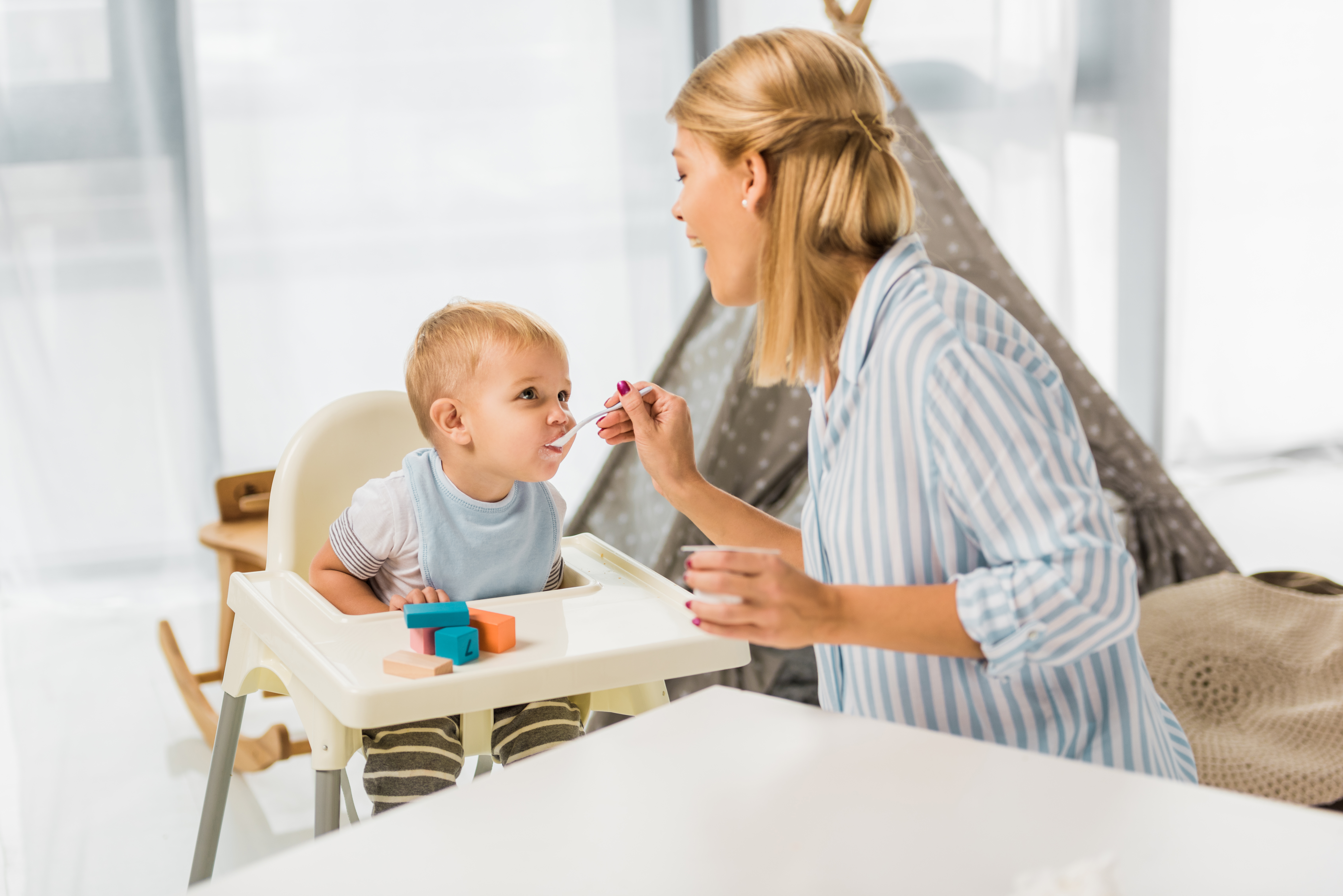 mom feeding son in highchair with baby food
